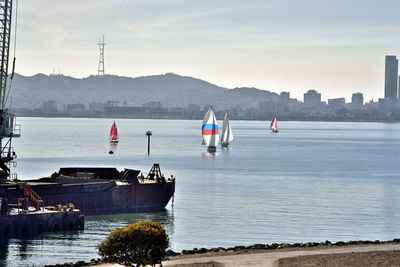 Boats sailing on river by city against sky