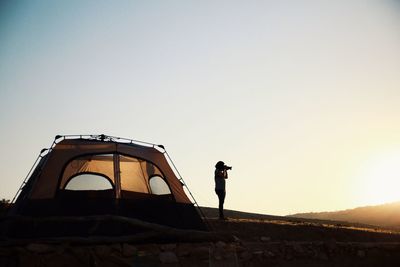 Low angle view of woman photographing against clear sky