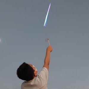 Rear view of boy holding kite against sky