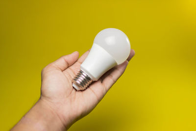 Close-up of hand holding cup against yellow background