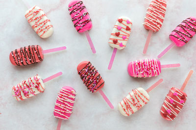 Several valentine cakesicles scattered on a pink marble surface.