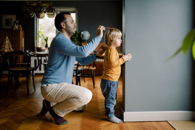 Full length of father measuring daughter's height against wall at home