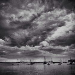 Sailboats in sea against cloudy sky