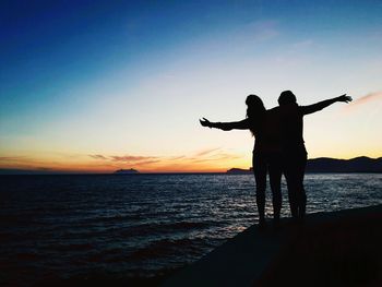 Silhouette people on beach against sky during sunset