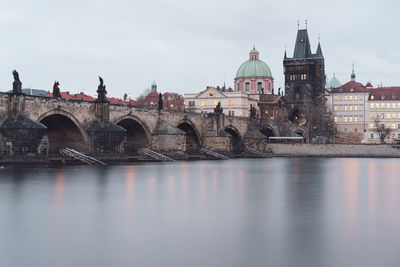 Bridge over river by buildings in city against sky