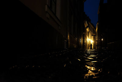 Illuminated street amidst buildings against sky at night