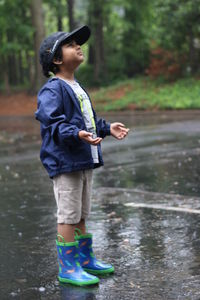Full length of boy in raincoat looking up while standing on road during rainy season