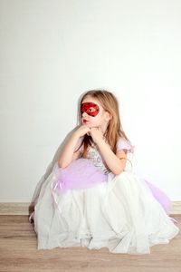 Portrait of young woman sitting against white wall