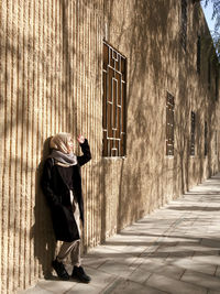 Full length of woman standing on footpath against  building with urban architecture wall