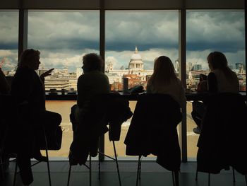 Rear view of people sitting by window in city