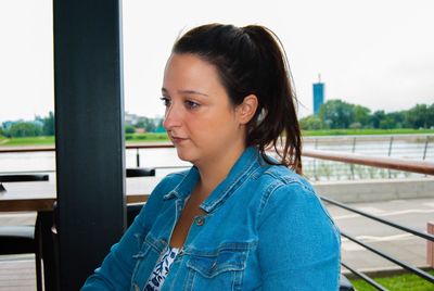 Portrait of young woman looking away while sitting on railing