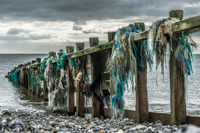 Fishing nets hanging on groyne at beach against cloudy sky