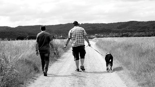 Rear view of father and dog walking on road