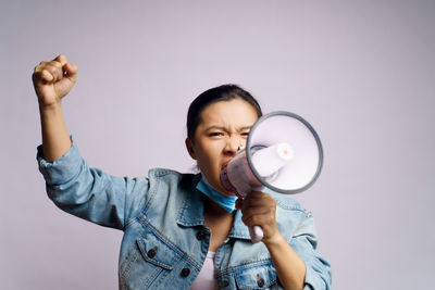 Close-up of young woman wearing flu mask screaming on megaphone against white background