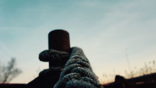 Low angle view of rope tied to bollard against sky during sunset
