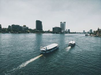 Boats in sea by buildings in city against sky