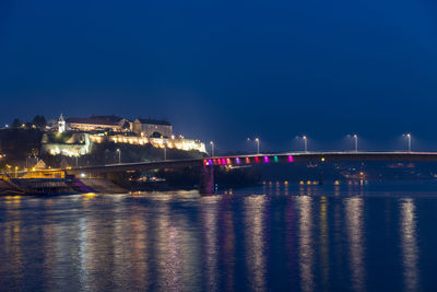 Illuminated bridge over river against sky at night