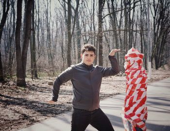 Portrait of young man gesturing by cordon tape wrapped woman on road in forest