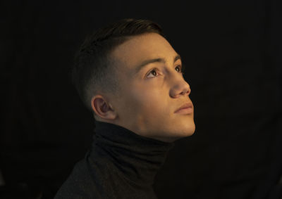 Close-up of young man looking away against black background