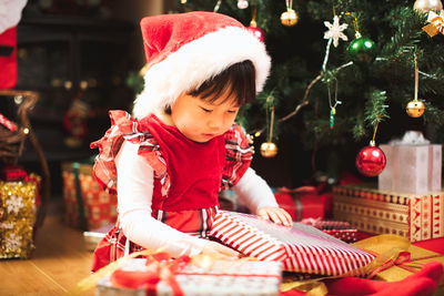 Girl opening gift while siting by christmas tree