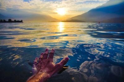 Close-up of hand on beach against sky during sunset