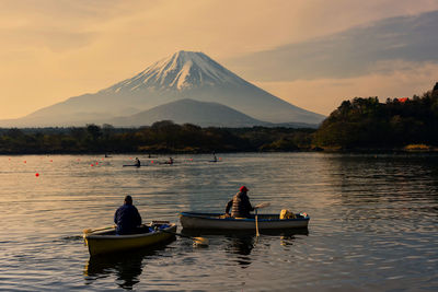 People on boat in lake against sky during sunset