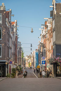 People walking on road amidst buildings in city against sky