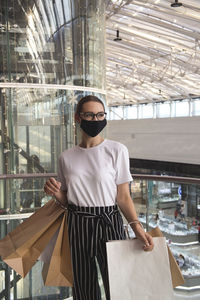 Beautiful young girl with paper bags with purchases near the shopping mall in the sunlight 