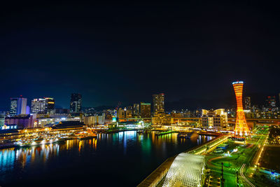 Illuminated buildings by river against sky at night