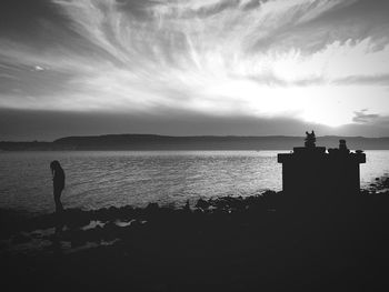 Silhouette woman standing at sea shore against sky