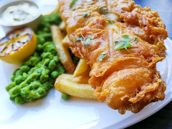 Close-up of fish with french fries and green peace served with dip in plate of table