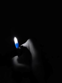 Close-up of hand holding lit candle in darkroom