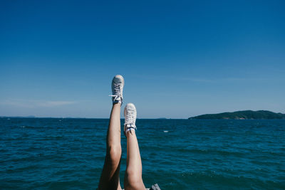 Low section of woman by sea against blue sky