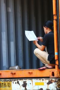 Side view of man sitting on metal structure