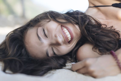 Cheerful woman with eyes closed lying at beach