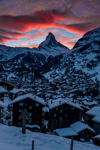 Snow covered houses and buildings against sky during sunset