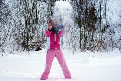 Happy woman playing with snow on field against bare trees