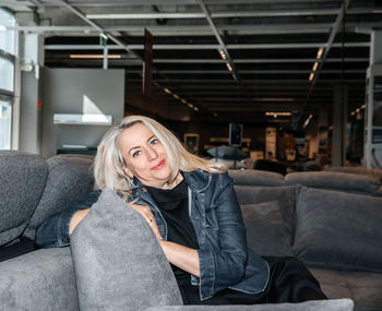 Joyful silver-haired lady in a dark denim jacket nestled on a charcoal sofa