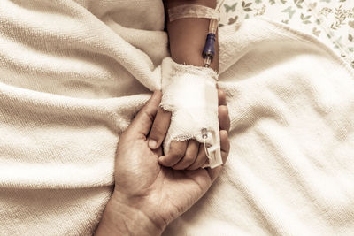 Cropped hand holding woman with iv drip on bed at hospital