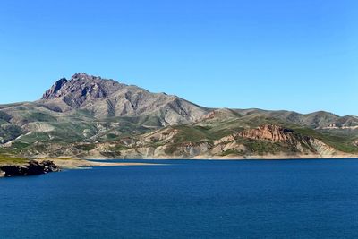 Scenic view of sea and mountains against clear blue sky