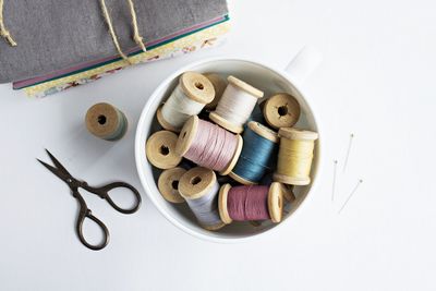 Directly above shot of thread spools in mug by textiles on table