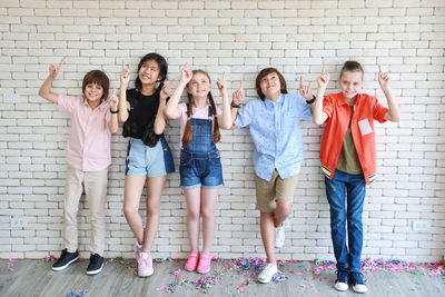 Full length portrait of happy friends standing against brick wall