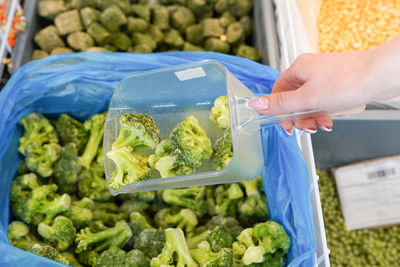 Women hand pick up frozen broccoli in supermarket.