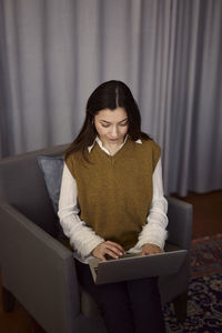 Woman using laptop on armchair