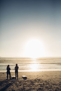 Silhouette people standing on beach against sky during sunset