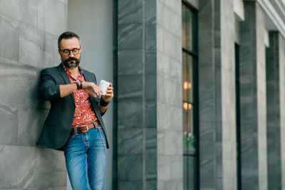 Young man leaning on wall having coffee