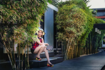 Full length portrait of woman sitting against trees