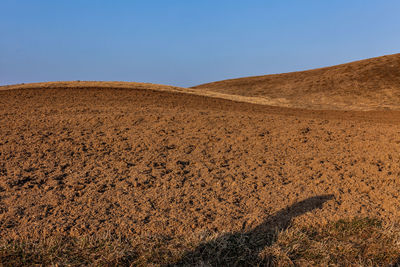 Plowed red earth fields on the background of the blue sky with a shadow in the foreground