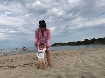Mother and baby boy walking on beach against sky