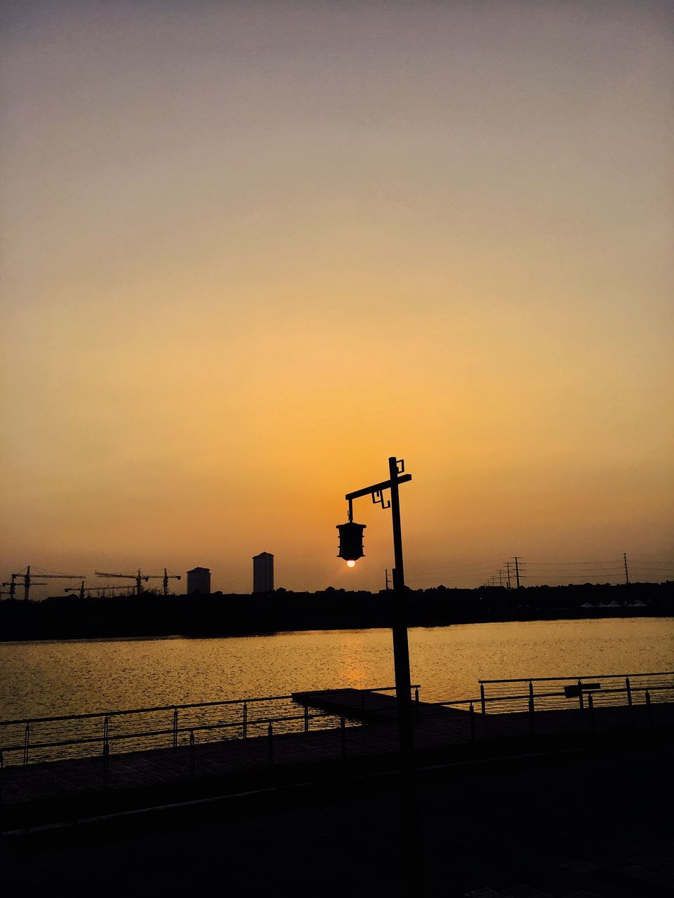 silhouette, sunset, water, calm, orange color, ocean, sea, tranquil scene, tranquility, railing, scenics, commercial dock, river, outdoors, lamp post, outline, sun, nature, sky, no people, beauty in nature
